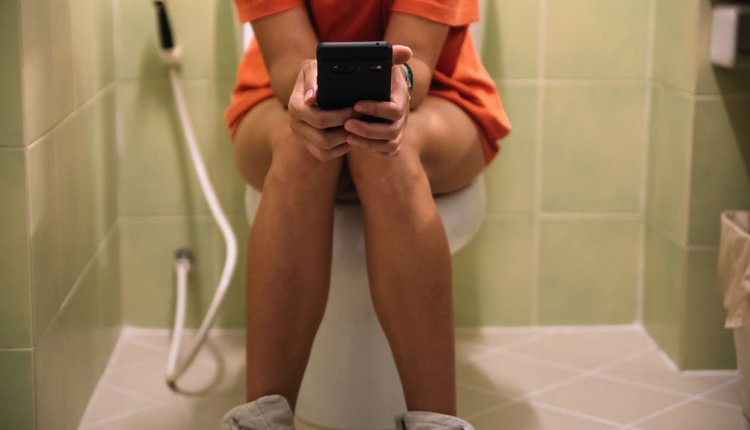 Vrouw met mobieltje zit op toilet