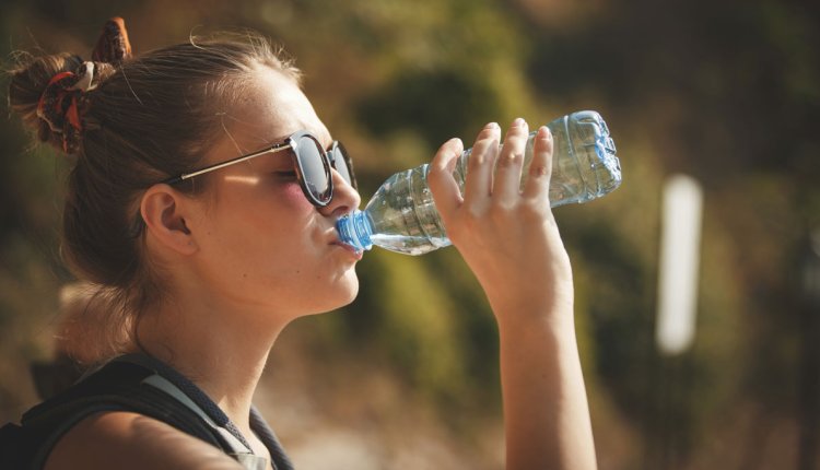 Jonge vrouw met zonnebril drinkt water uit flesje