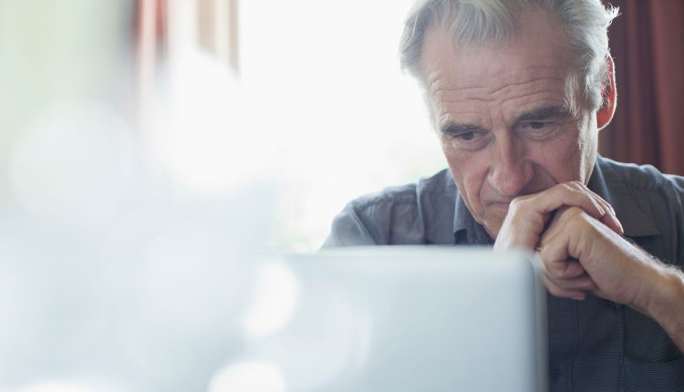 Man bedachtzaam achter computer met handen gevouwen