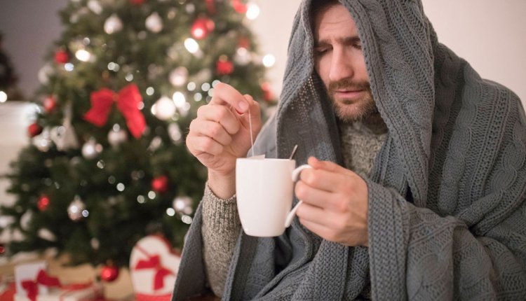 Man zit met een griepje ziek te zijn bij de kerstboom met een kop thee