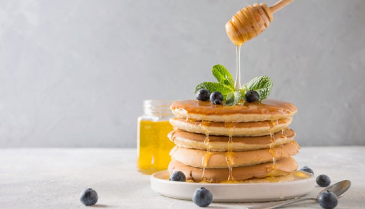 Stapel pannenkoekjes waar honing overheen wordt gegoten