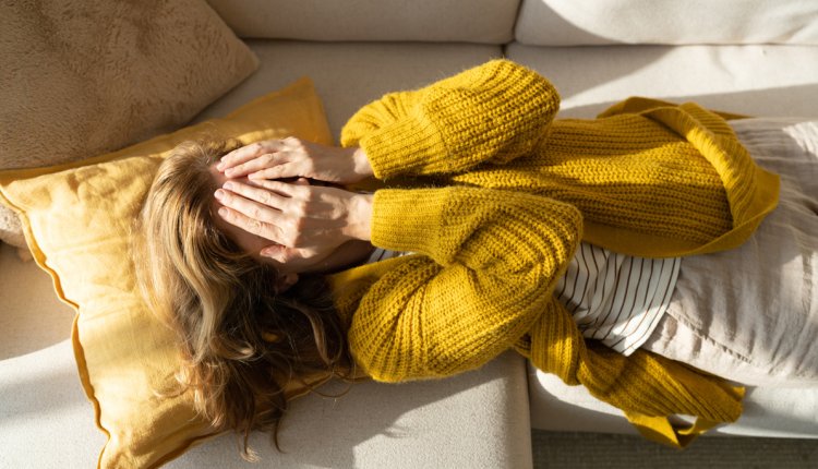 Vrouw ligt met handen voor haar ogen op de bank 