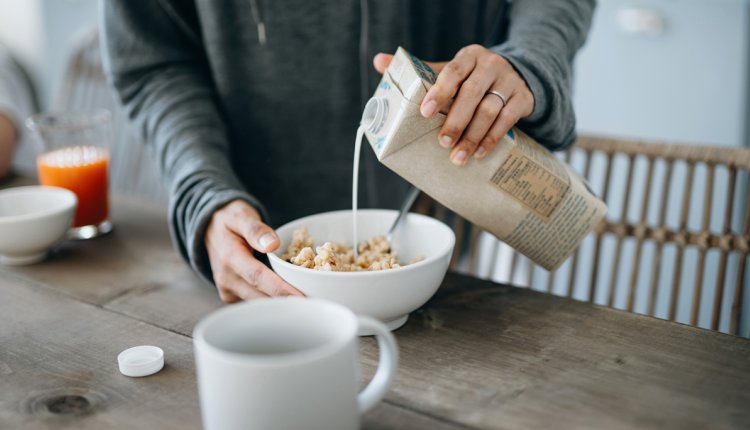 Vrouw schenkt havermelk of haverdrank in een kom met muesli