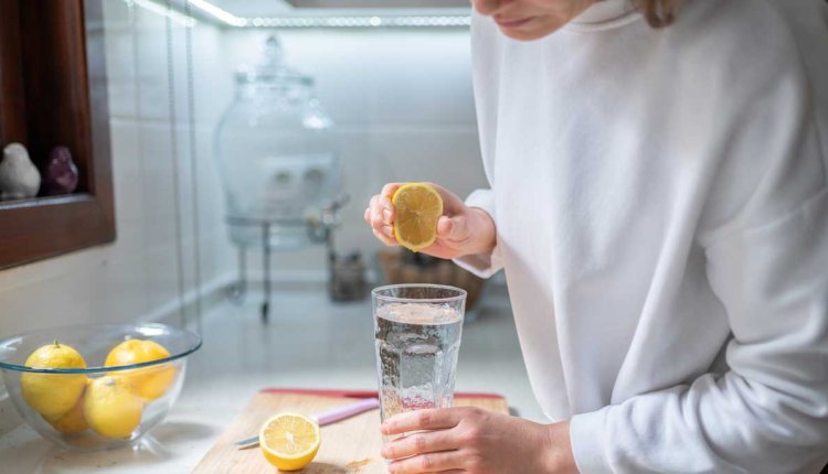 Vrouw perst citroen uit boven glas water