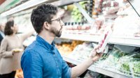 Man in supermarkt leest verpakking van product in het koelvak