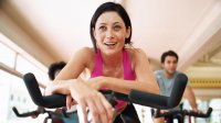 Vrouw in de sportschool op een spinningfiets, met waterfles in de hand