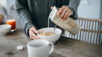 Vrouw schenkt havermelk of haverdrank in een kom met muesli