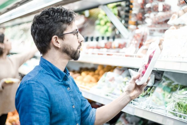 Man in supermarkt leest verpakking van product in het koelvak