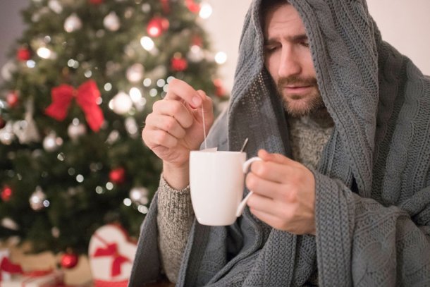 Man zit met een griepje ziek te zijn bij de kerstboom met een kop thee