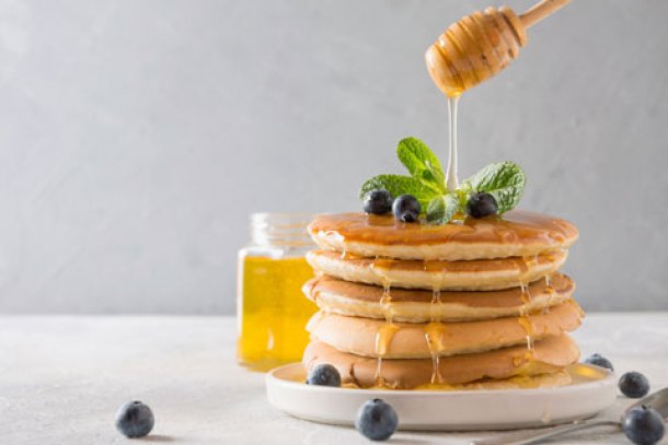 Stapel pannenkoekjes waar honing overheen wordt gegoten