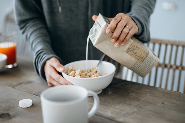 Vrouw schenkt havermelk of haverdrank in een kom met muesli