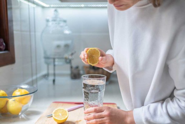 Vrouw perst citroen uit boven glas water